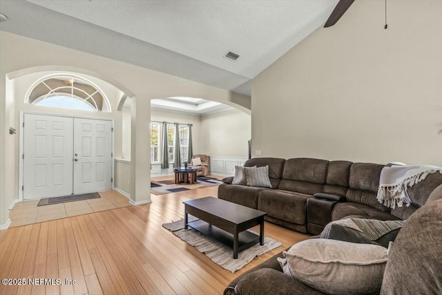 living room featuring lofted ceiling, baseboards, arched walkways, light wood-style floors, and visible vents