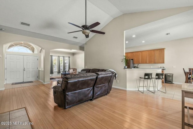 living room with high vaulted ceiling, baseboards, arched walkways, ceiling fan, and light wood-style flooring