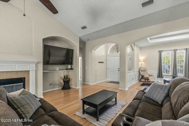 living area featuring light wood-style flooring, visible vents, arched walkways, and lofted ceiling