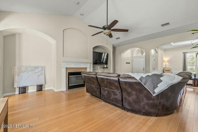 living room with lofted ceiling, arched walkways, ceiling fan, light wood-style flooring, and a tile fireplace
