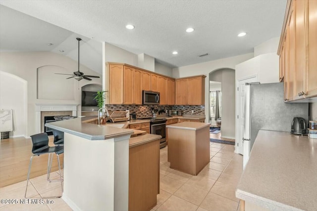 kitchen with vaulted ceiling, arched walkways, ceiling fan, a peninsula, and appliances with stainless steel finishes