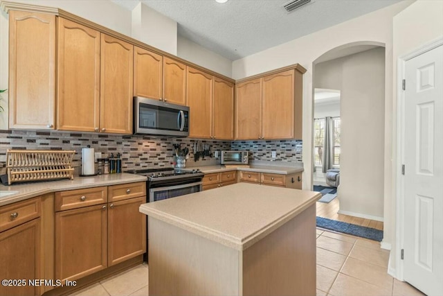 kitchen featuring light countertops, stainless steel appliances, light tile patterned floors, visible vents, and arched walkways