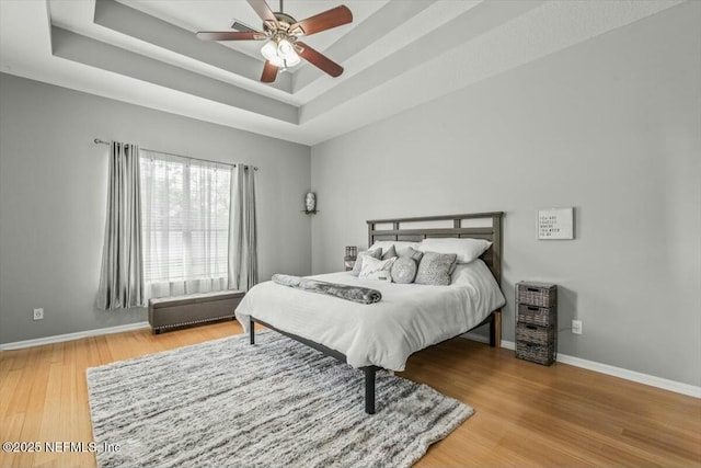 bedroom with a tray ceiling, baseboards, wood finished floors, and a ceiling fan