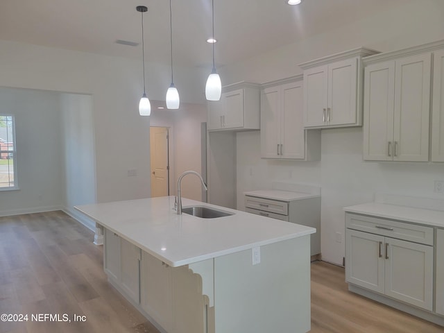 kitchen with light wood-type flooring, sink, and an island with sink