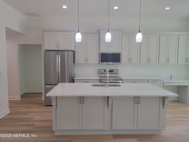 kitchen with light wood finished floors, a sink, hanging light fixtures, light countertops, and appliances with stainless steel finishes