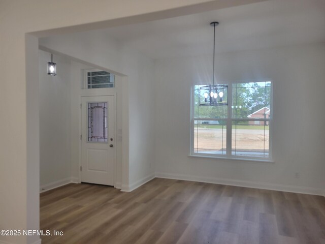 unfurnished dining area featuring baseboards, a notable chandelier, and wood finished floors