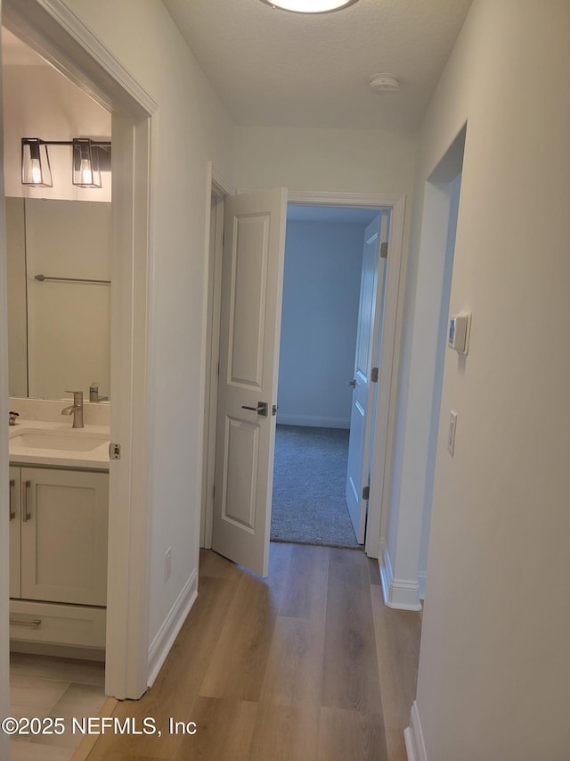 hallway with a sink, baseboards, and light wood finished floors