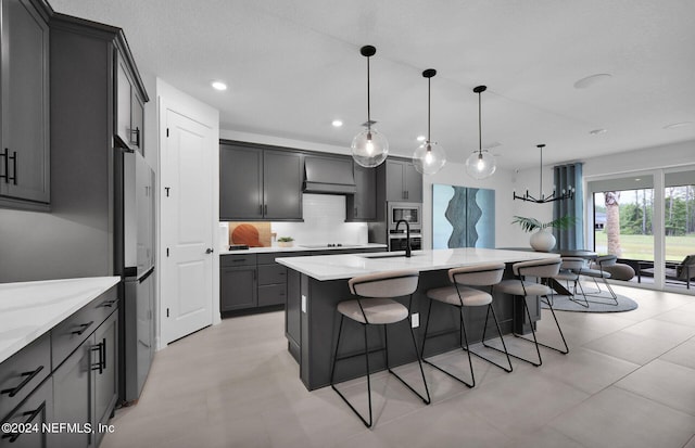 kitchen featuring gray cabinetry, stainless steel appliances, a kitchen island with sink, sink, and decorative light fixtures