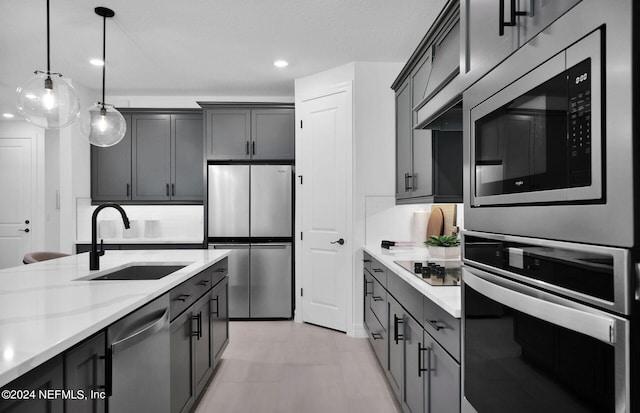 kitchen with appliances with stainless steel finishes, light stone counters, gray cabinetry, sink, and hanging light fixtures