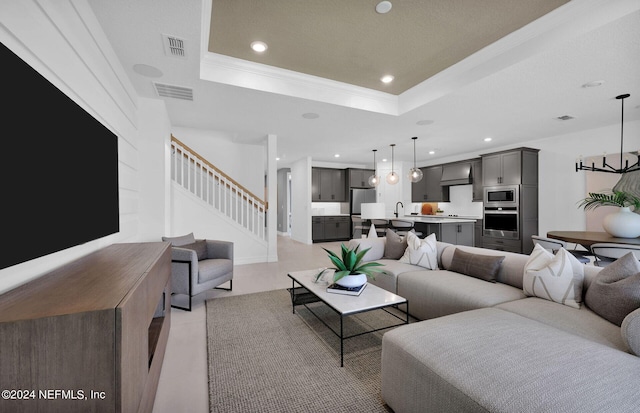 living room with a raised ceiling, crown molding, and sink