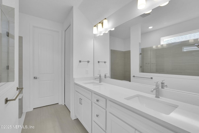 bathroom with double vanity, tiled shower, a sink, and visible vents