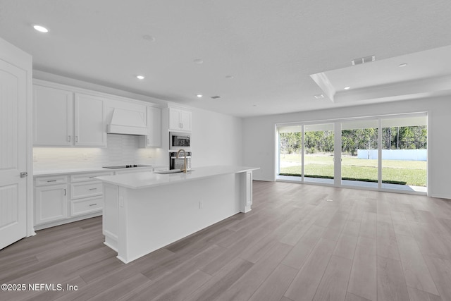 kitchen featuring black electric stovetop, custom range hood, visible vents, a sink, and built in microwave