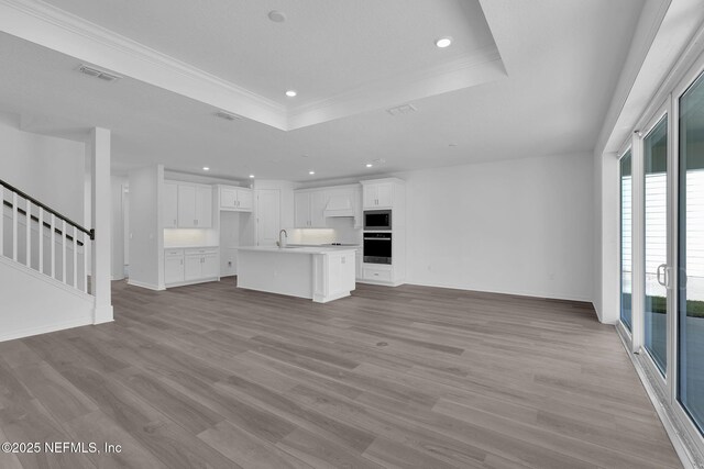 unfurnished living room with a tray ceiling, light wood finished floors, visible vents, a sink, and stairs