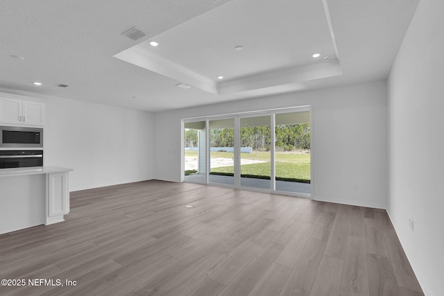 unfurnished living room with light wood finished floors, a tray ceiling, and visible vents