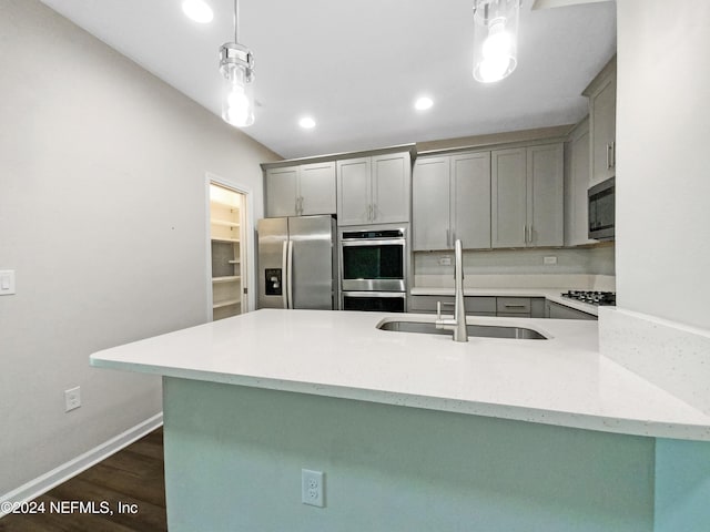 kitchen featuring sink, hanging light fixtures, stainless steel appliances, dark wood-type flooring, and kitchen peninsula