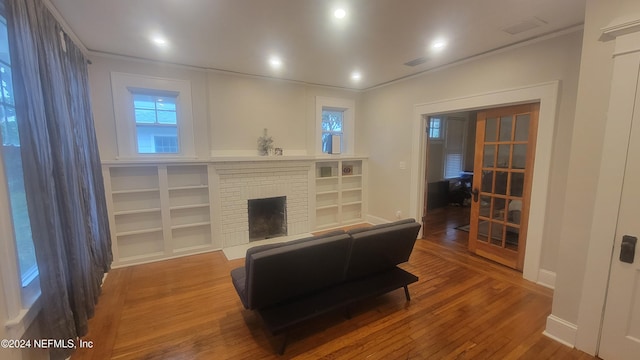 living room featuring crown molding, a fireplace, visible vents, wood finished floors, and baseboards