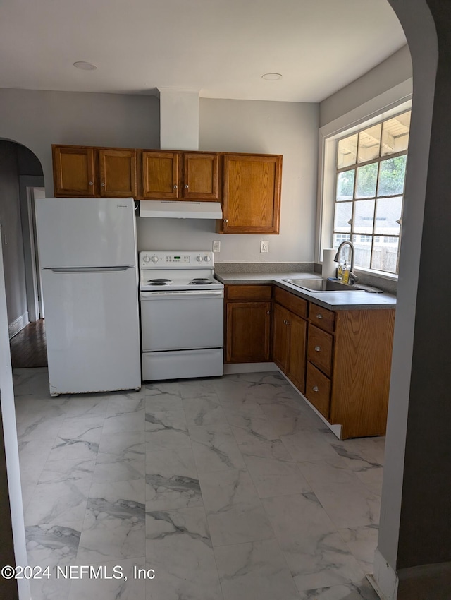 kitchen with white appliances, arched walkways, brown cabinets, under cabinet range hood, and a sink