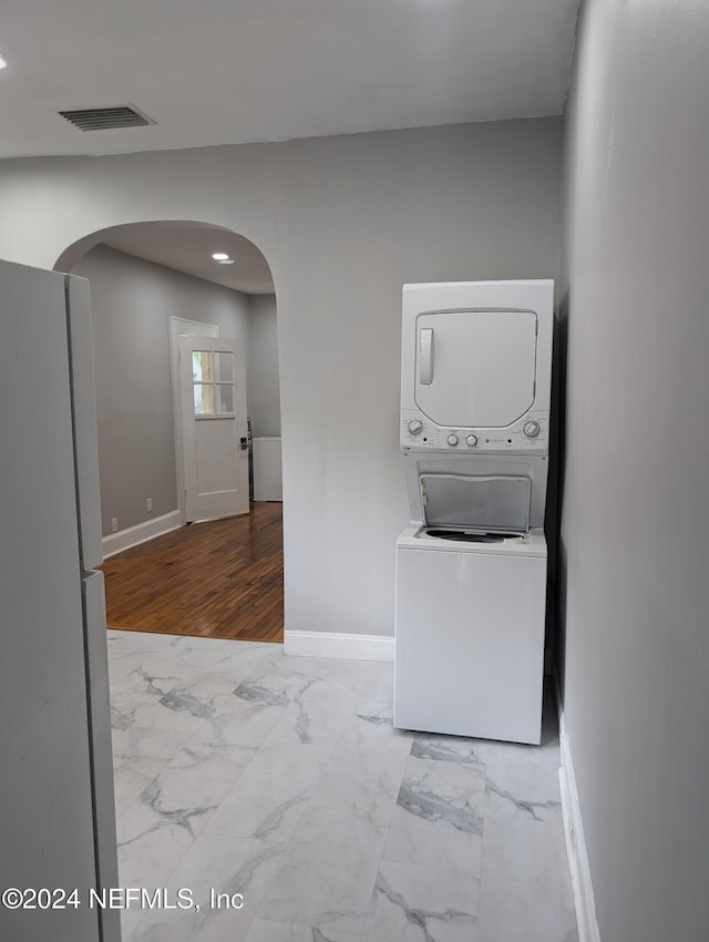 clothes washing area with arched walkways, visible vents, baseboards, stacked washer / drying machine, and marble finish floor