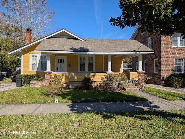 view of front of house with a front yard, covered porch, roof with shingles, and a chimney