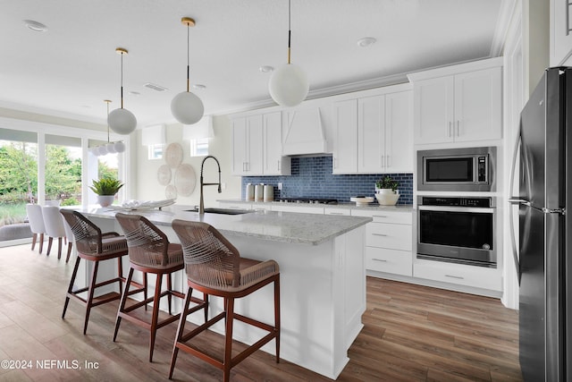 kitchen featuring a kitchen island with sink, sink, stainless steel appliances, and decorative light fixtures