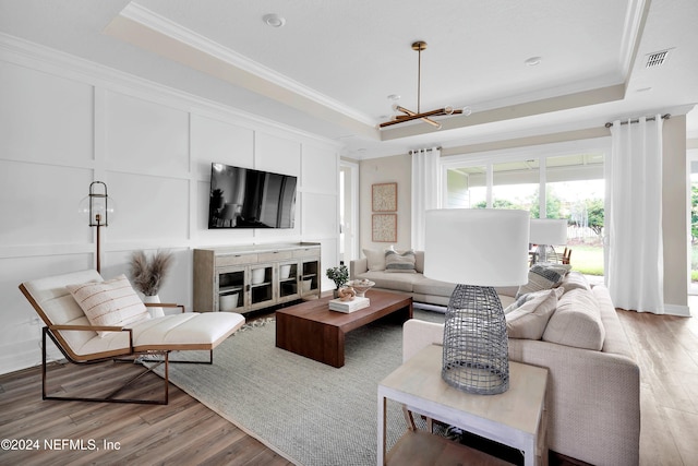 living room featuring a raised ceiling, ornamental molding, and light hardwood / wood-style flooring