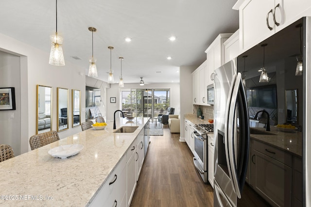 kitchen with backsplash, appliances with stainless steel finishes, open floor plan, white cabinets, and a sink