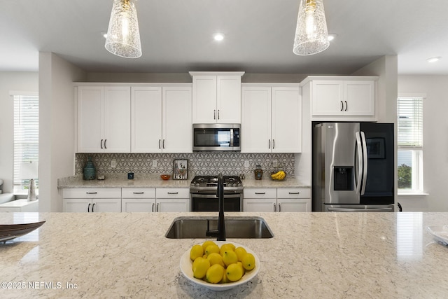 kitchen with white cabinets, appliances with stainless steel finishes, light stone counters, and pendant lighting