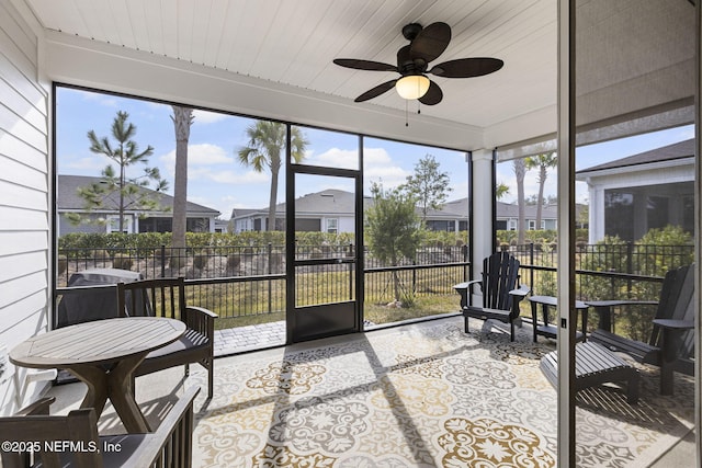 sunroom with a ceiling fan, a residential view, wood ceiling, and plenty of natural light