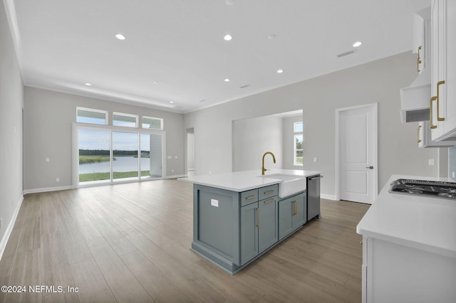 kitchen with appliances with stainless steel finishes, a kitchen island with sink, sink, light hardwood / wood-style flooring, and white cabinets