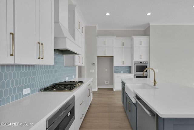 kitchen featuring premium range hood, crown molding, light hardwood / wood-style flooring, appliances with stainless steel finishes, and white cabinetry