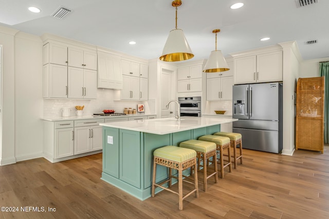 kitchen with pendant lighting, a kitchen island with sink, sink, decorative backsplash, and stainless steel appliances