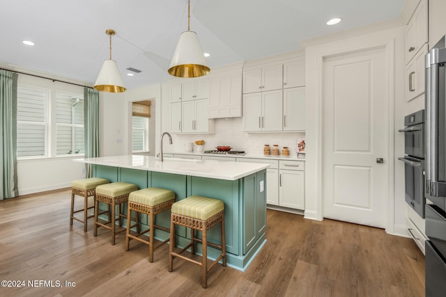 kitchen with a breakfast bar, sink, a center island with sink, white cabinetry, and hanging light fixtures