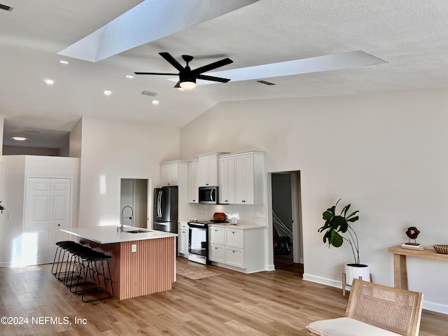 kitchen featuring white cabinetry, stainless steel appliances, light hardwood / wood-style floors, a breakfast bar area, and a kitchen island with sink