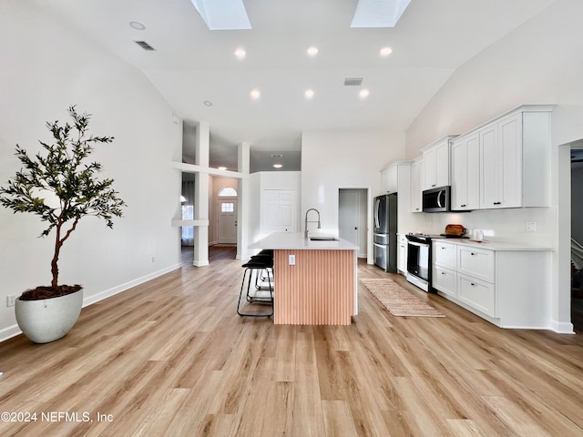 kitchen featuring a breakfast bar, a skylight, light wood-type flooring, an island with sink, and stainless steel appliances