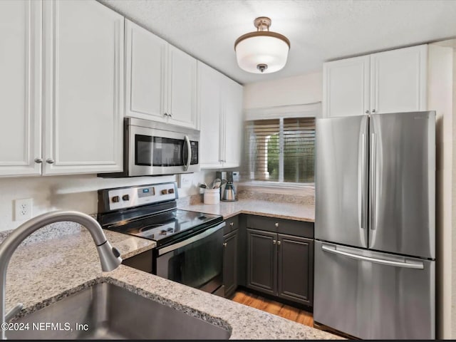 kitchen with sink, light hardwood / wood-style flooring, appliances with stainless steel finishes, light stone countertops, and white cabinets