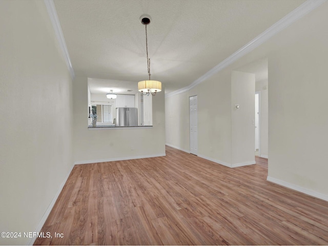 unfurnished dining area featuring an inviting chandelier, ornamental molding, a textured ceiling, and light wood-type flooring