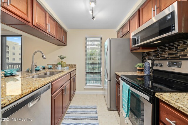 kitchen with decorative backsplash, light stone countertops, stainless steel appliances, sink, and light tile patterned floors