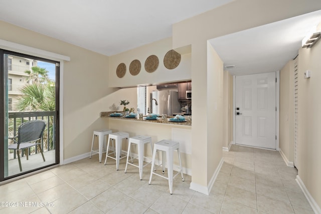 kitchen with a breakfast bar, kitchen peninsula, stainless steel appliances, and light tile patterned floors