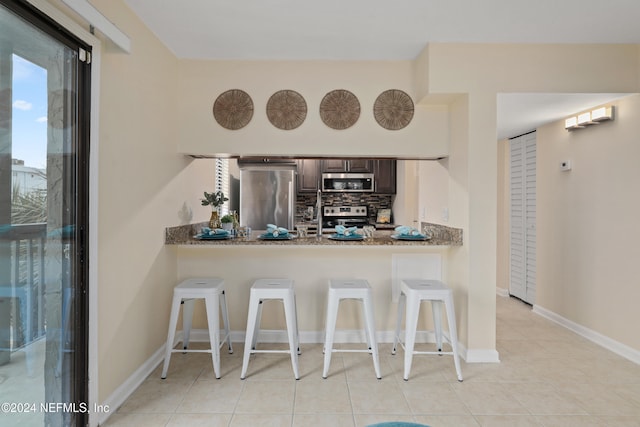 kitchen featuring dark brown cabinetry, kitchen peninsula, stainless steel appliances, and a breakfast bar