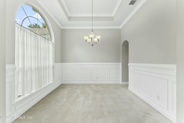 empty room with ornamental molding, light colored carpet, an inviting chandelier, and a tray ceiling