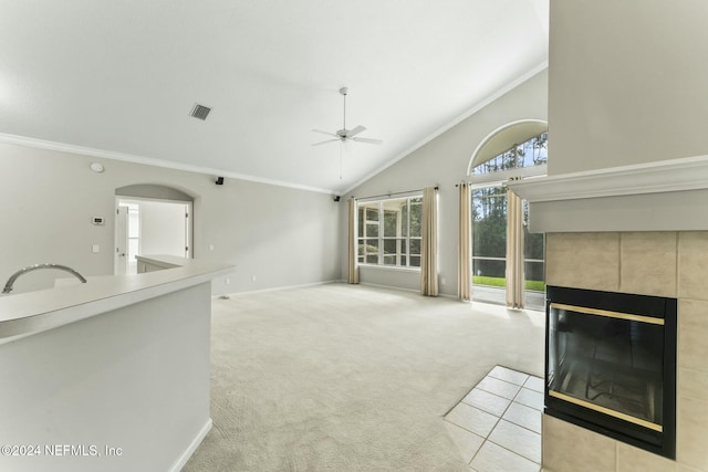 unfurnished living room featuring ceiling fan, sink, a tiled fireplace, light carpet, and ornamental molding