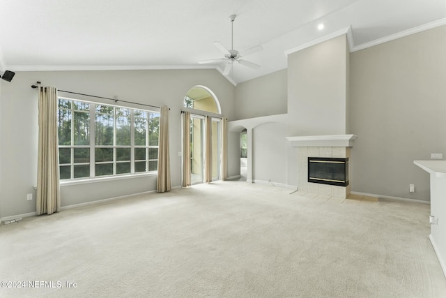 unfurnished living room featuring ceiling fan, high vaulted ceiling, crown molding, light colored carpet, and a tiled fireplace