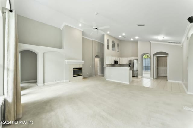 unfurnished living room with a tiled fireplace, light carpet, high vaulted ceiling, and ceiling fan