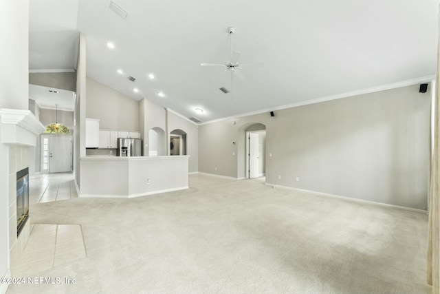 unfurnished living room with high vaulted ceiling, crown molding, ceiling fan, light colored carpet, and a tiled fireplace