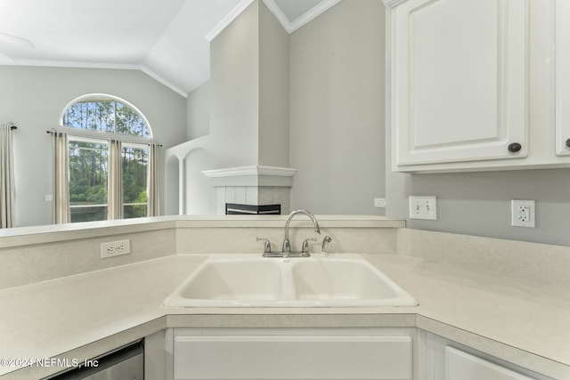 kitchen with a tile fireplace, sink, vaulted ceiling, ornamental molding, and white cabinetry