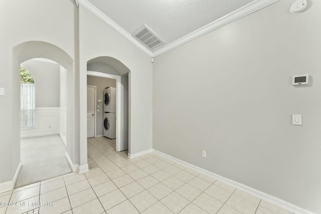 tiled spare room featuring crown molding, stacked washing maching and dryer, and a textured ceiling