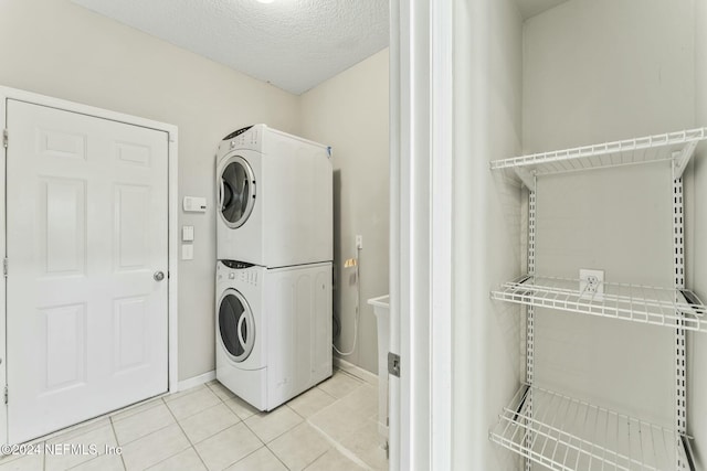 laundry area featuring a textured ceiling, stacked washer / drying machine, and light tile patterned flooring