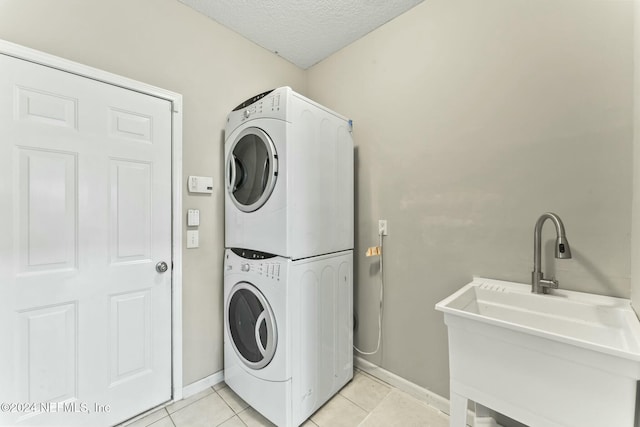 clothes washing area featuring light tile patterned flooring, sink, stacked washing maching and dryer, and a textured ceiling