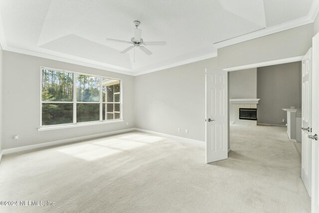 carpeted empty room with a tray ceiling, ceiling fan, ornamental molding, and a tiled fireplace