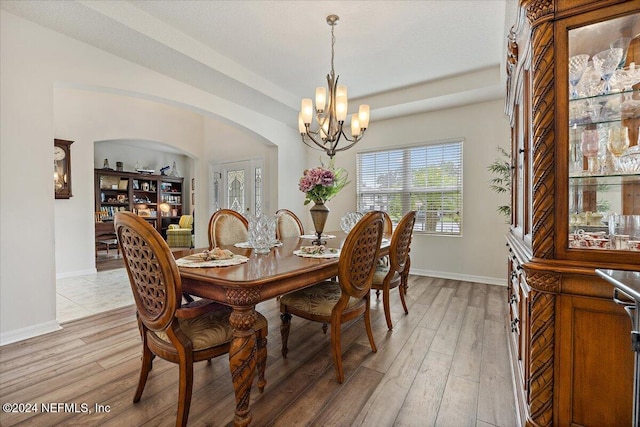 dining area with arched walkways, light wood-type flooring, baseboards, and a notable chandelier